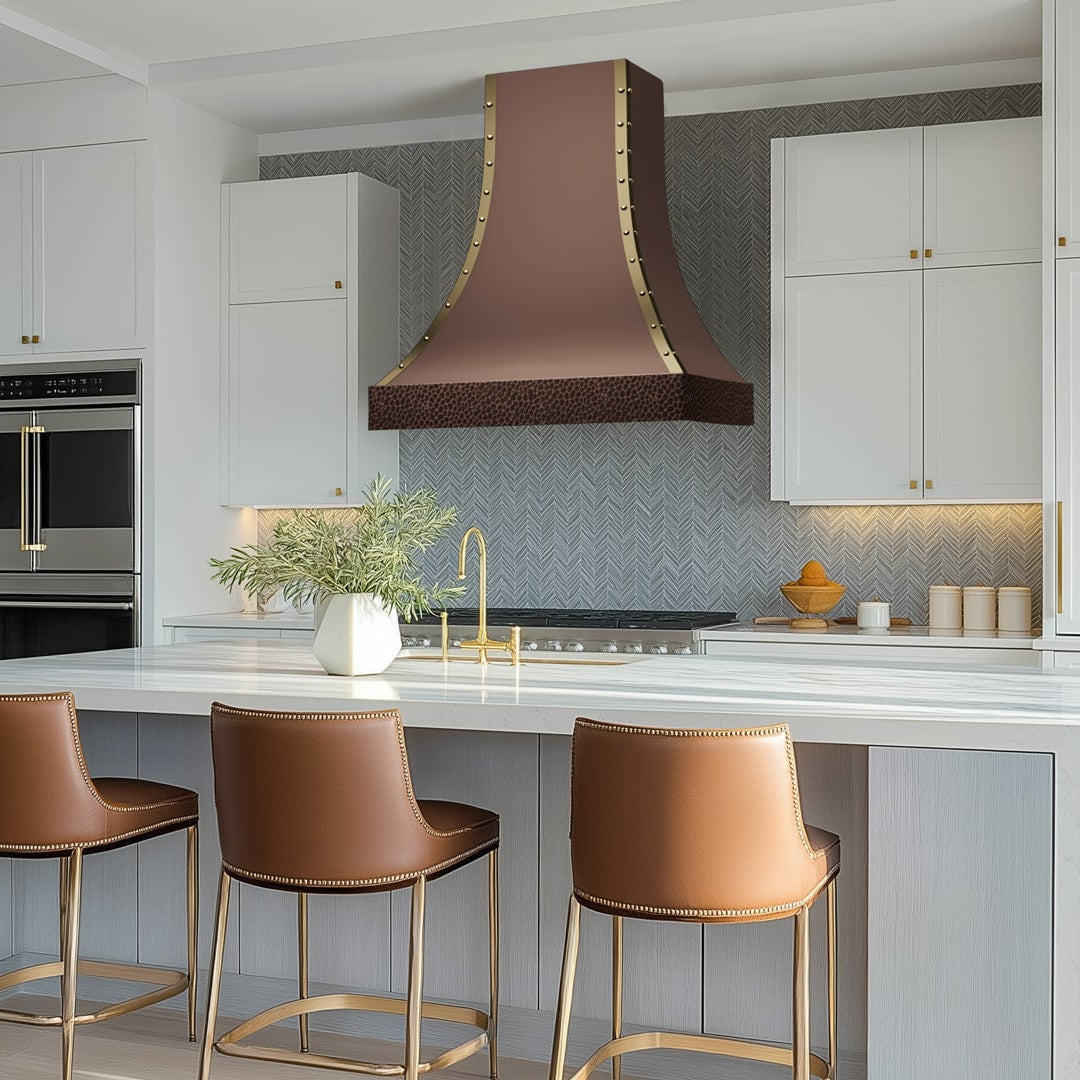 Copper hood with gold rivet trim, featuring a textured hammered base to elevate kitchen edge with white cabinetry with bar stools.
