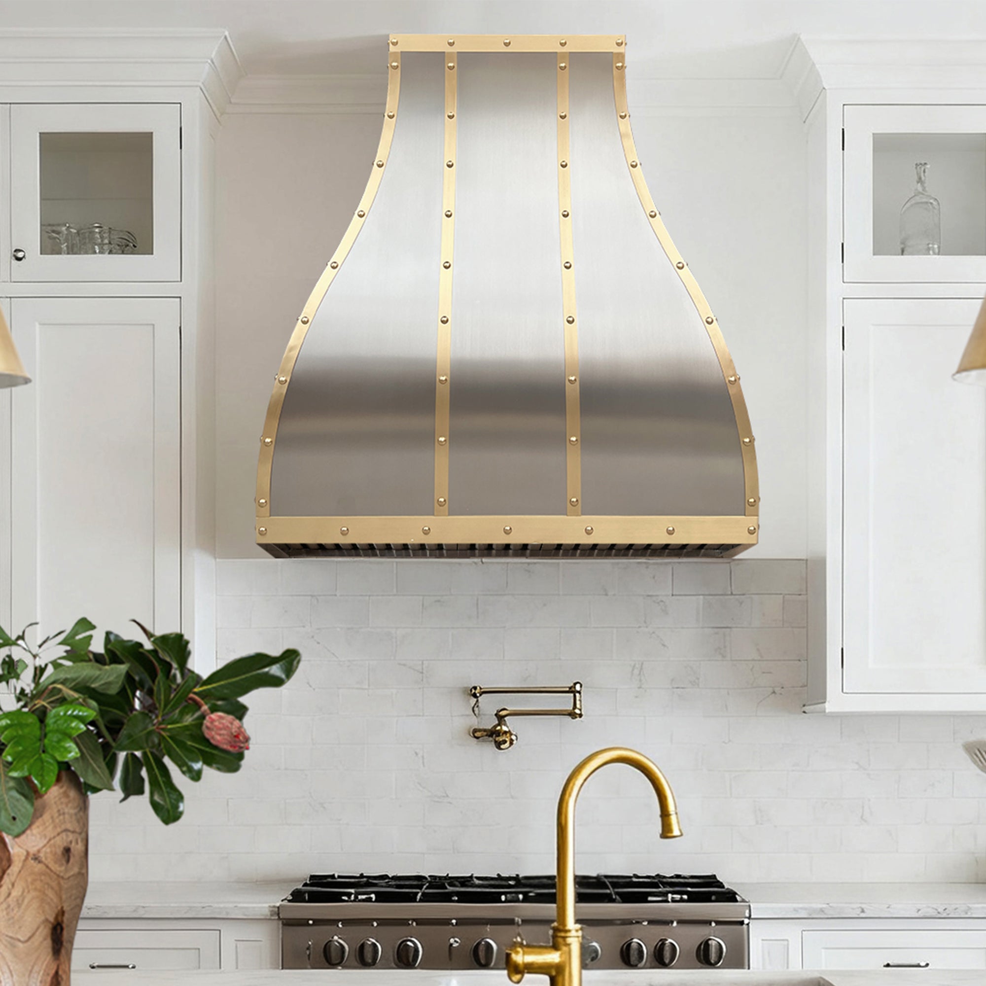 Modern kitchen with gold-range hood and faucet, white cabinets, and a plant.