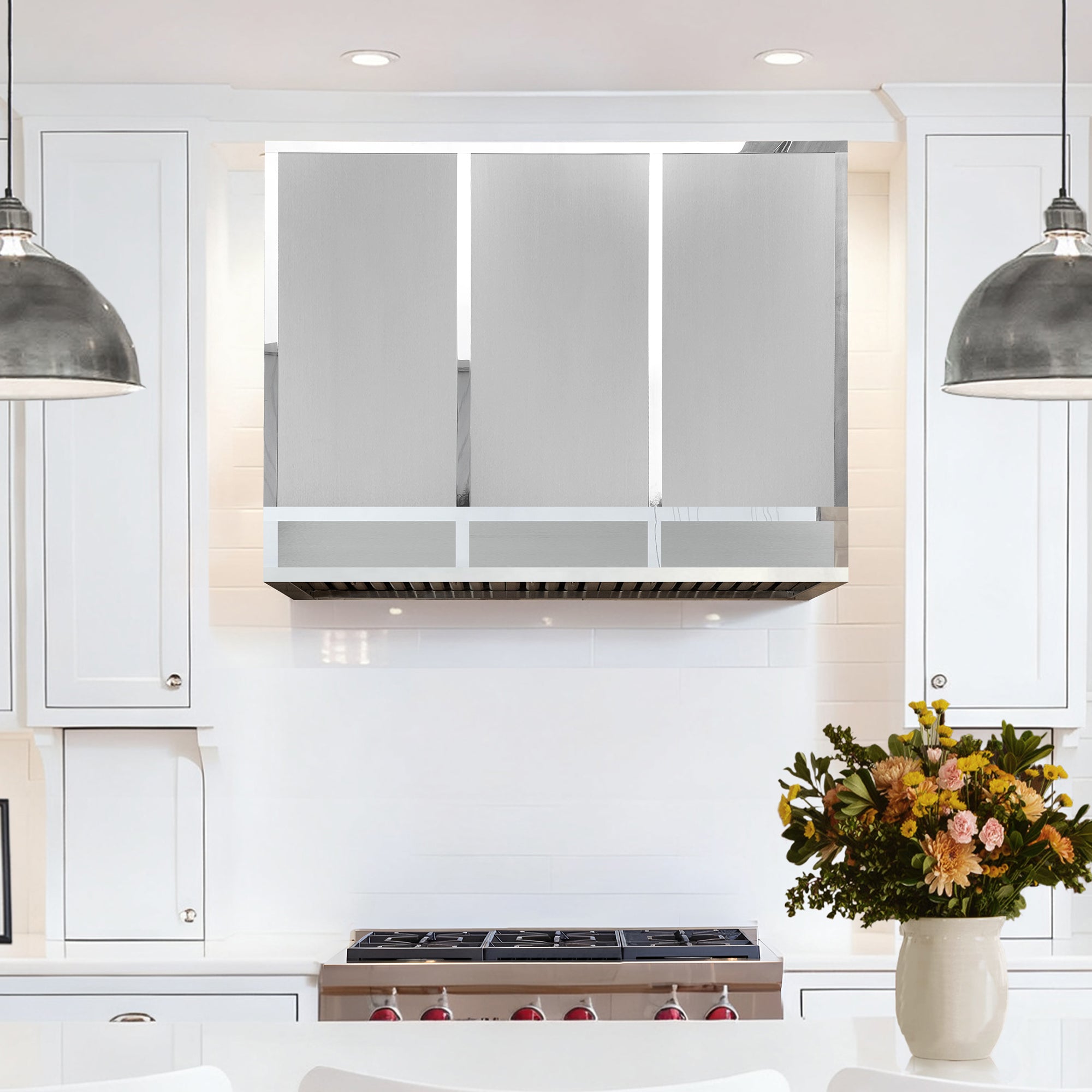 Modern kitchen with stainless steel range hood, white cabinets, and a vase of flowers on the counter.