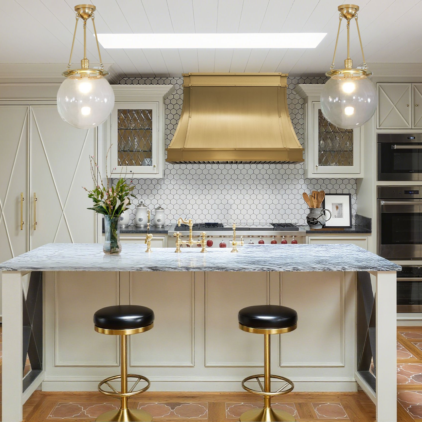 Modern kitchen with marble island, gold fixtures, and black stools.