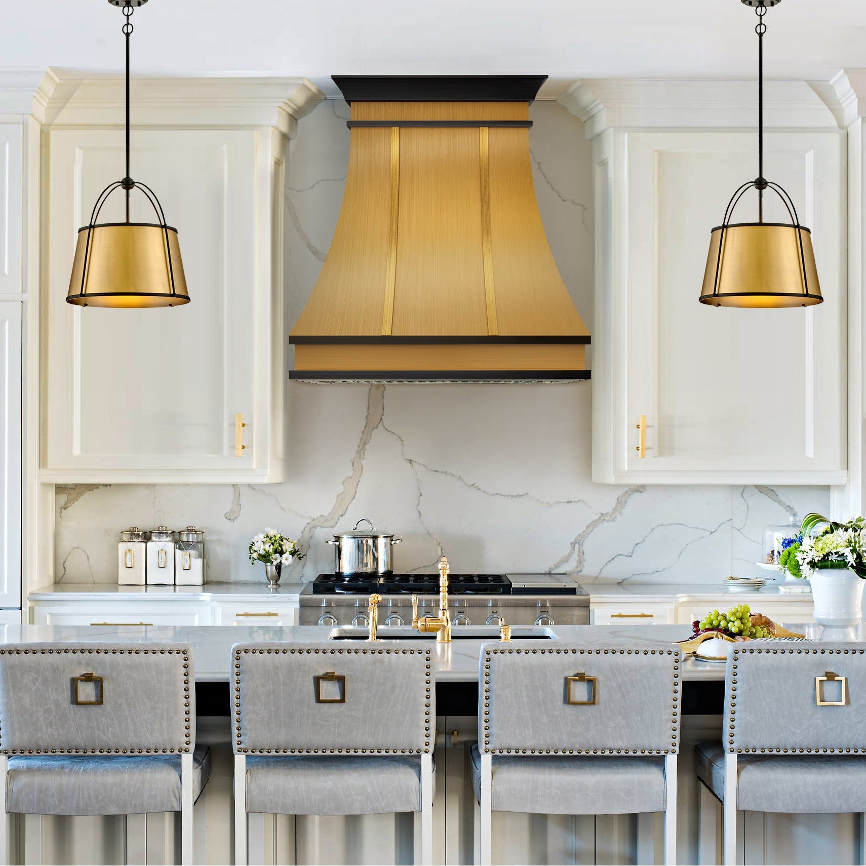 Double edged brass hood for Modern kitchen with white cabinets, marble island, and gold pendant lights.